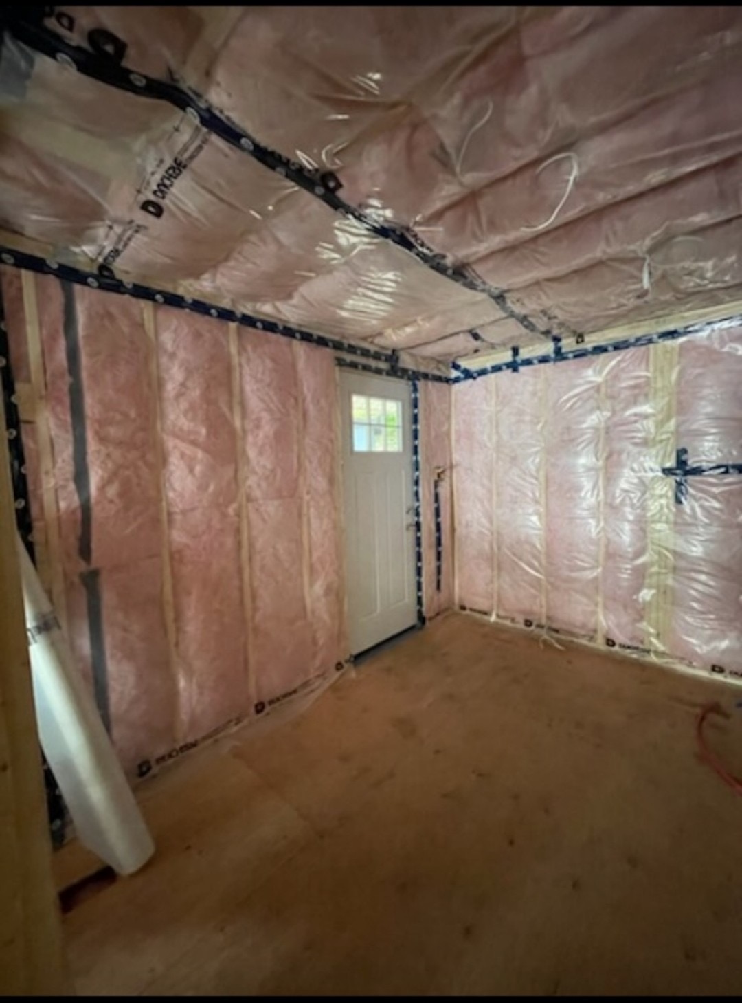 Room under construction with pink insulation, vapour barrier, and sealed exterior door