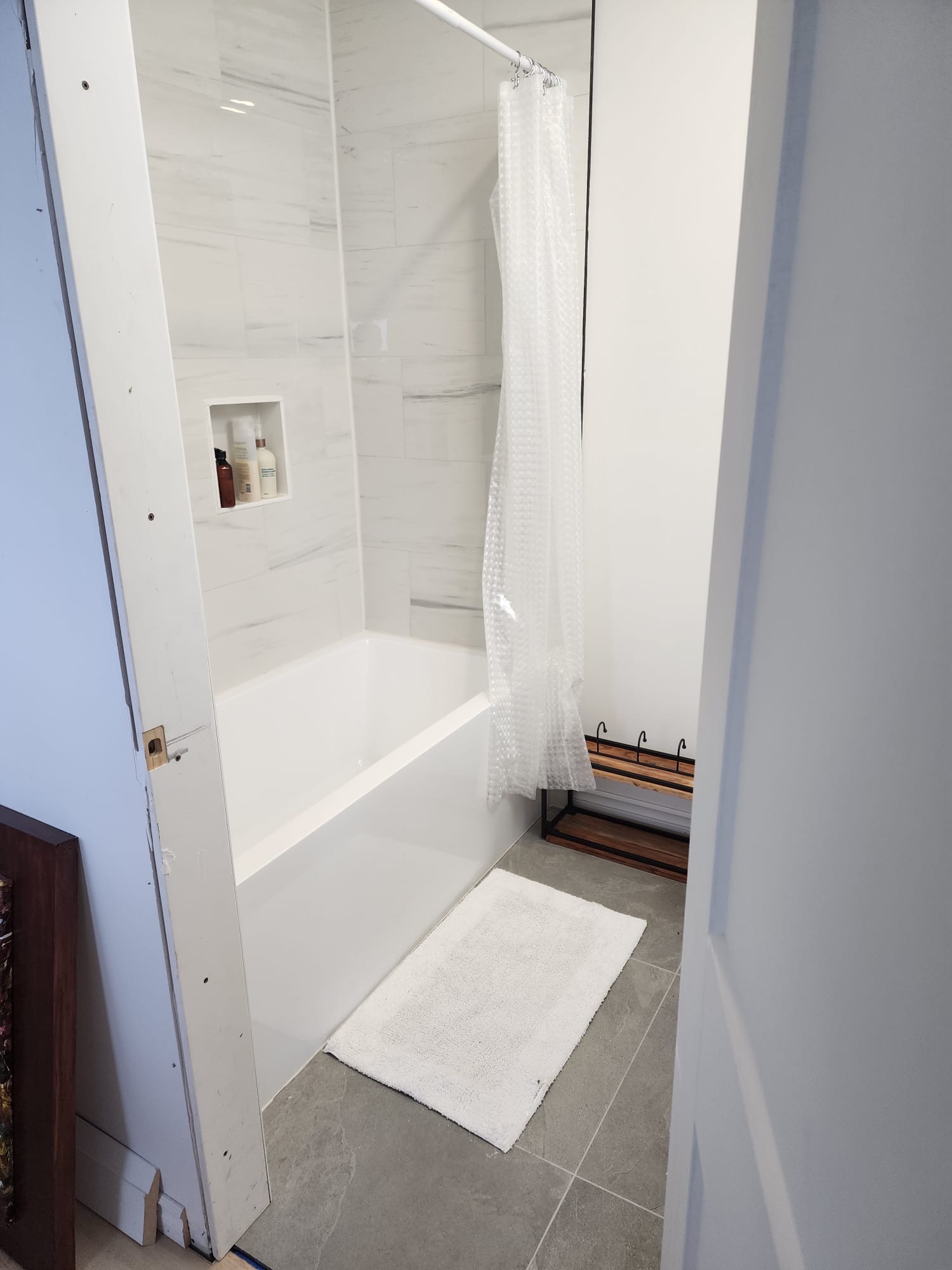 Bathtub surround with marble-look tile, glass shower partition, and white bath mat