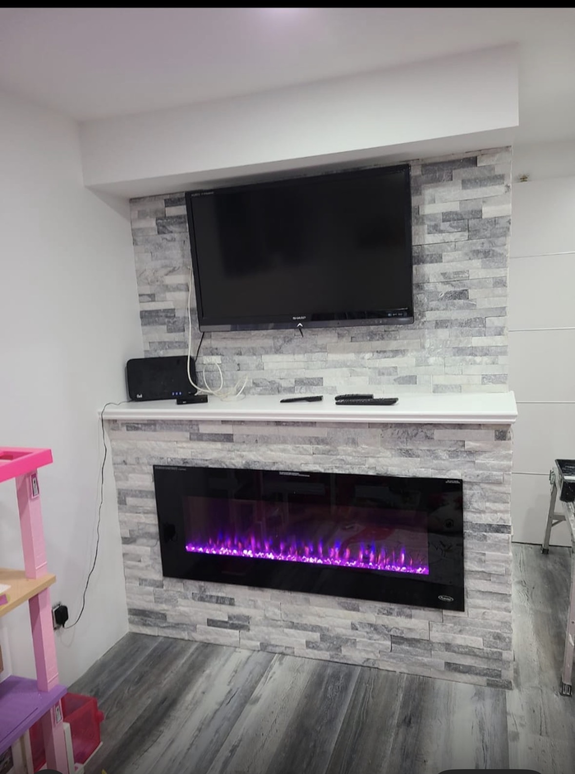Completed stacked stone fireplace feature wall with mounted TV and white mantel shelf