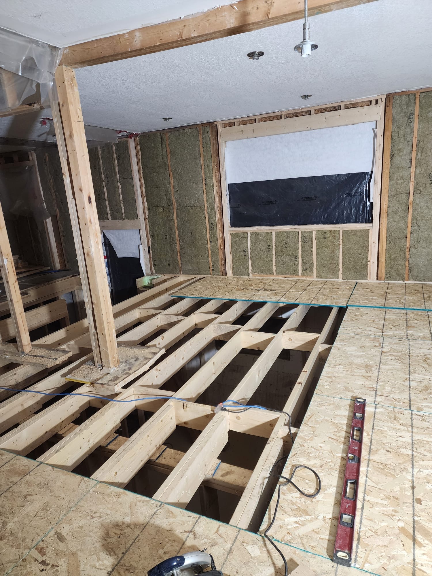 Interior subfloor framing with exposed joists and insulation in a renovation