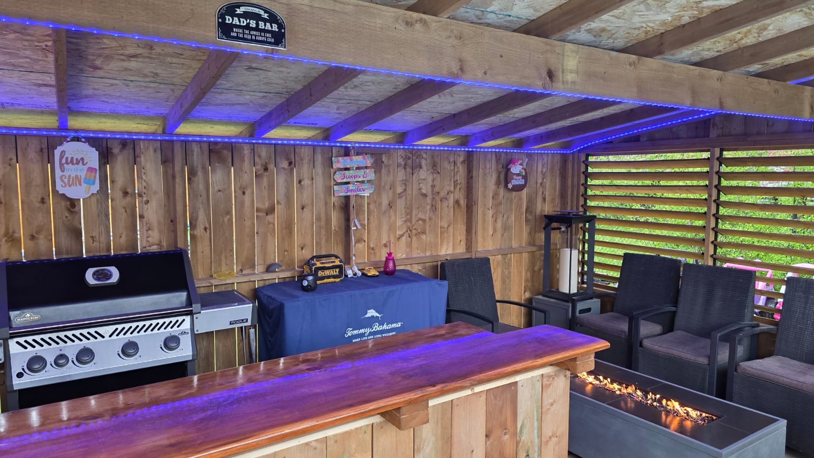 Covered outdoor bar with cedar counter, built-in grill, LED lighting, and fire table