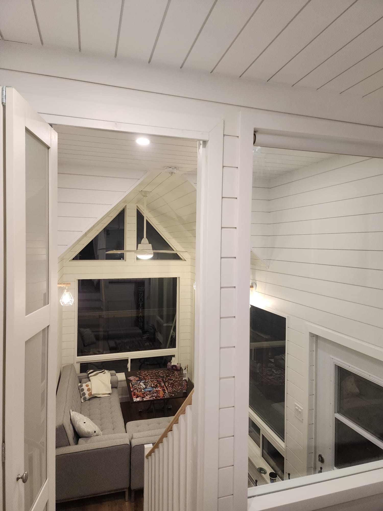 Loft view overlooking a vaulted living room with white shiplap walls and large windows