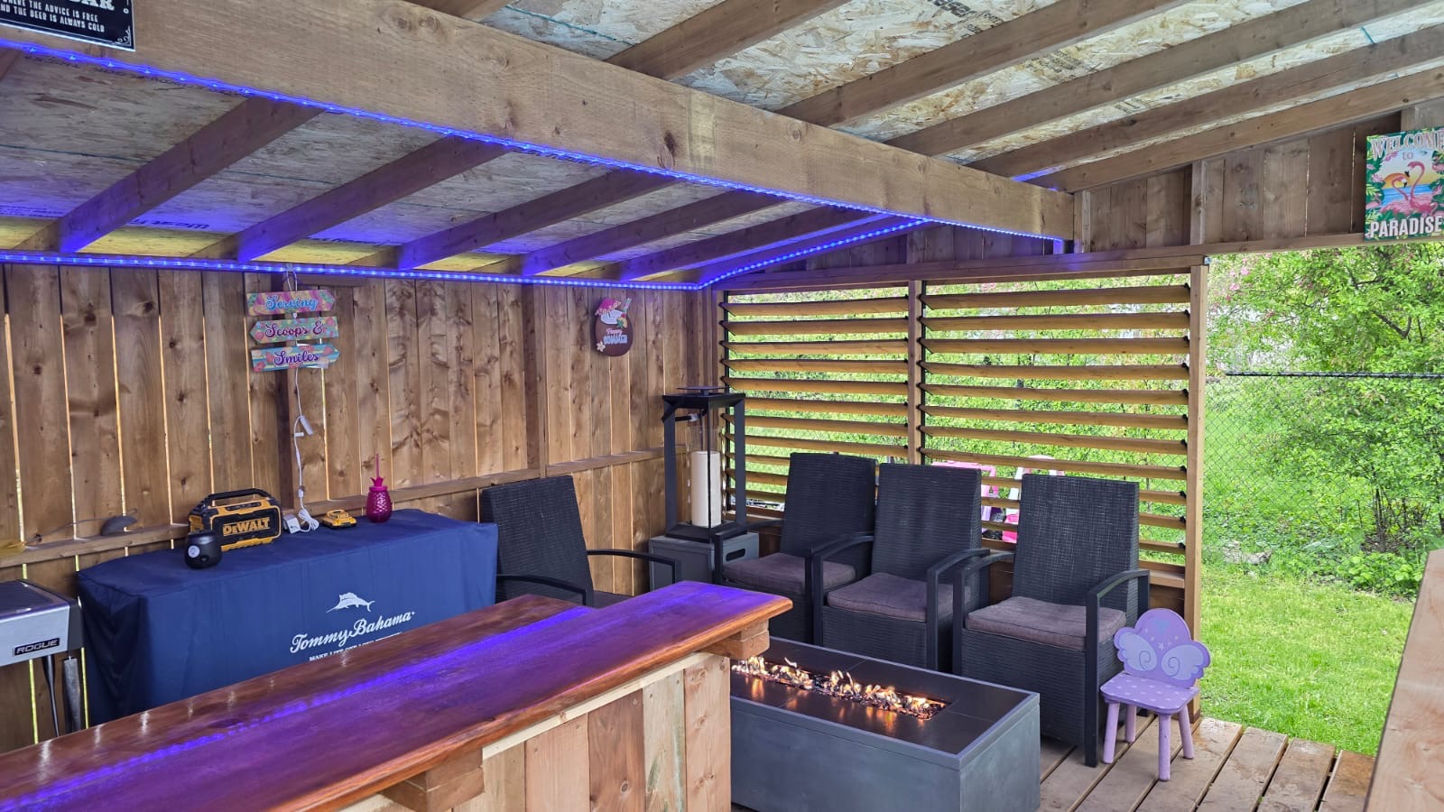 Covered outdoor bar lounge with cedar walls, LED lighting, fire table, and louvered privacy screen