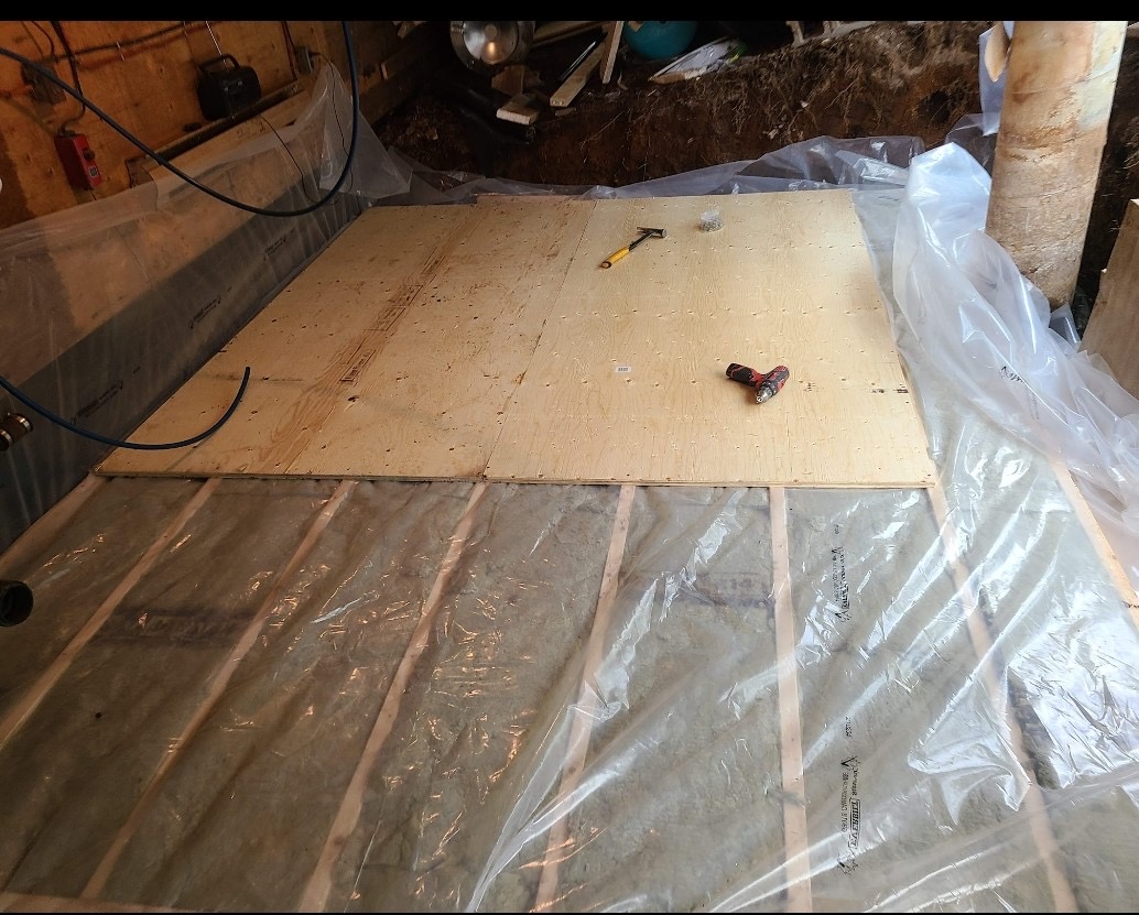 Plywood subfloor being installed over insulated basement floor framing