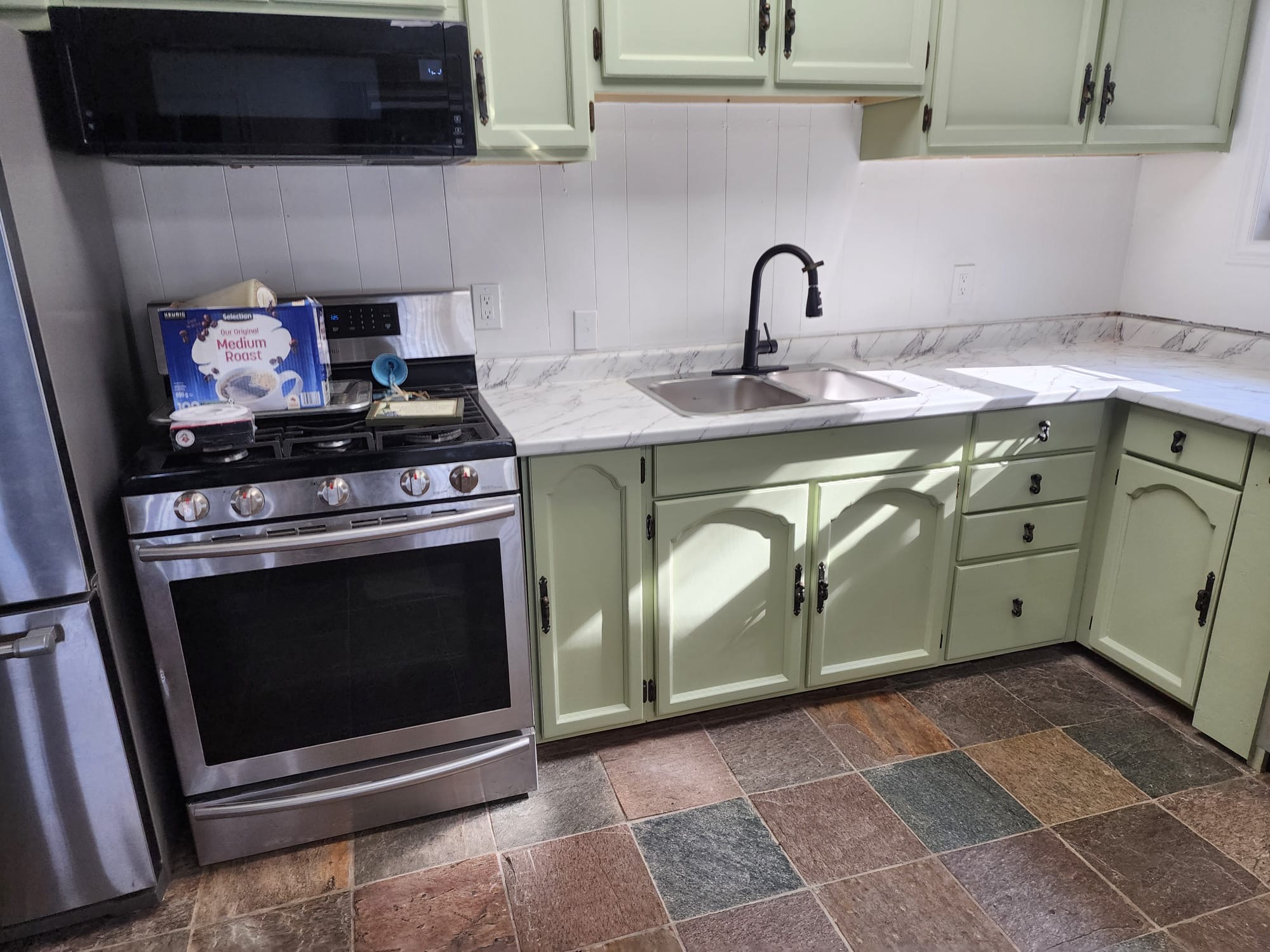 Refreshed kitchen with sage green cabinets, marble-look countertops, stainless stove, and black faucet