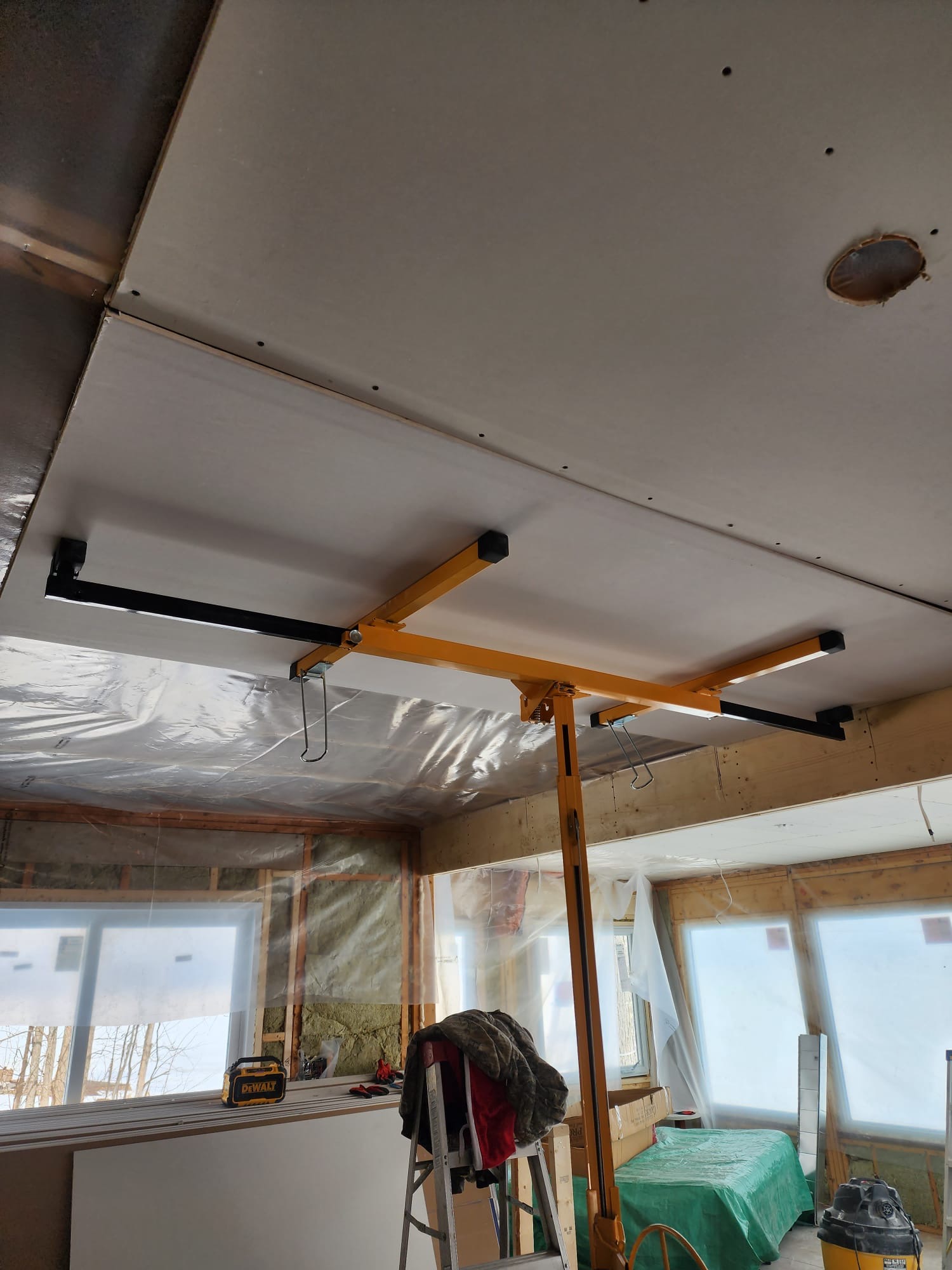 Ceiling drywall installation supported by a panel lift during room construction