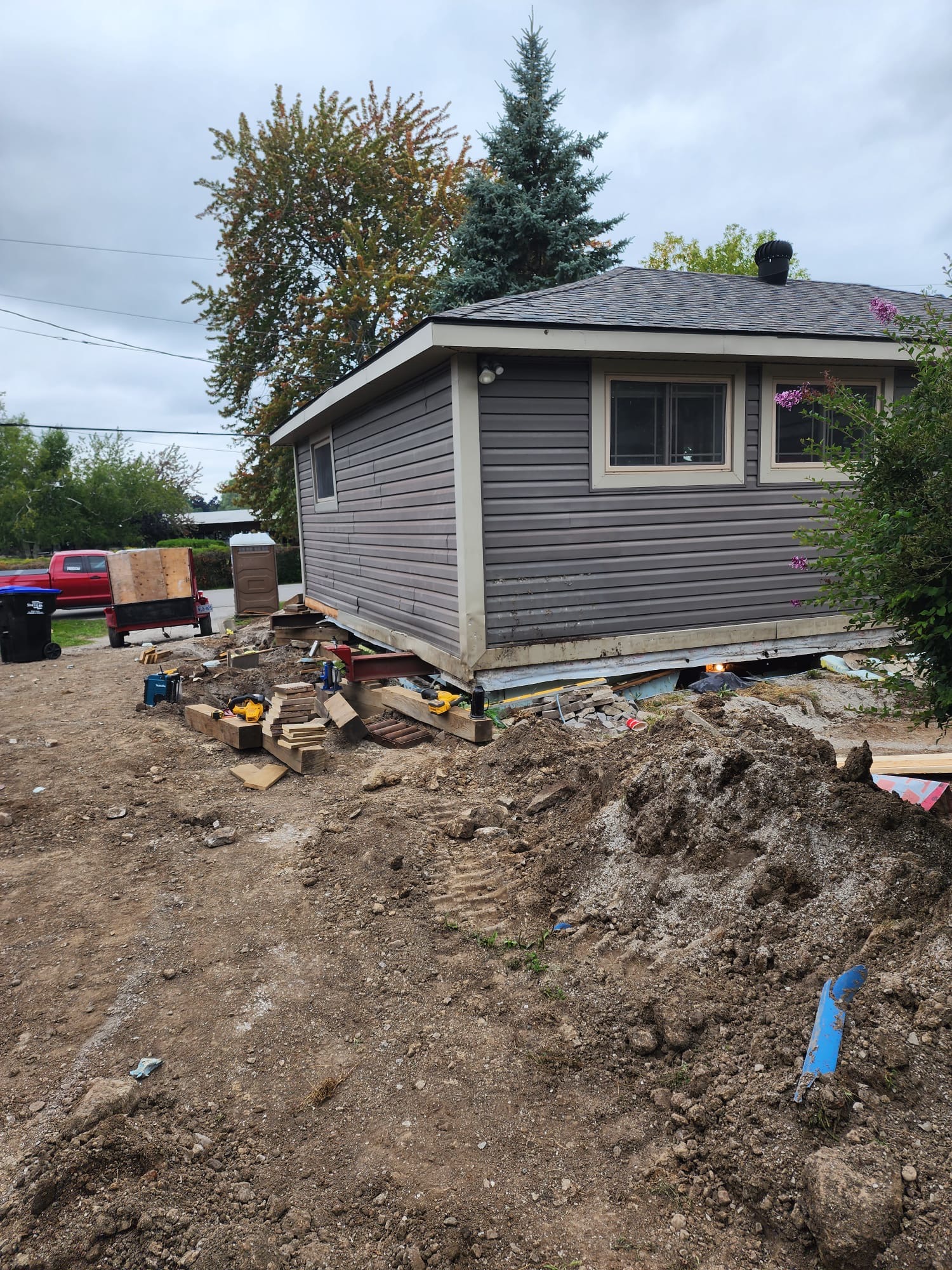 House raised on temporary supports with exposed foundation and siding underway