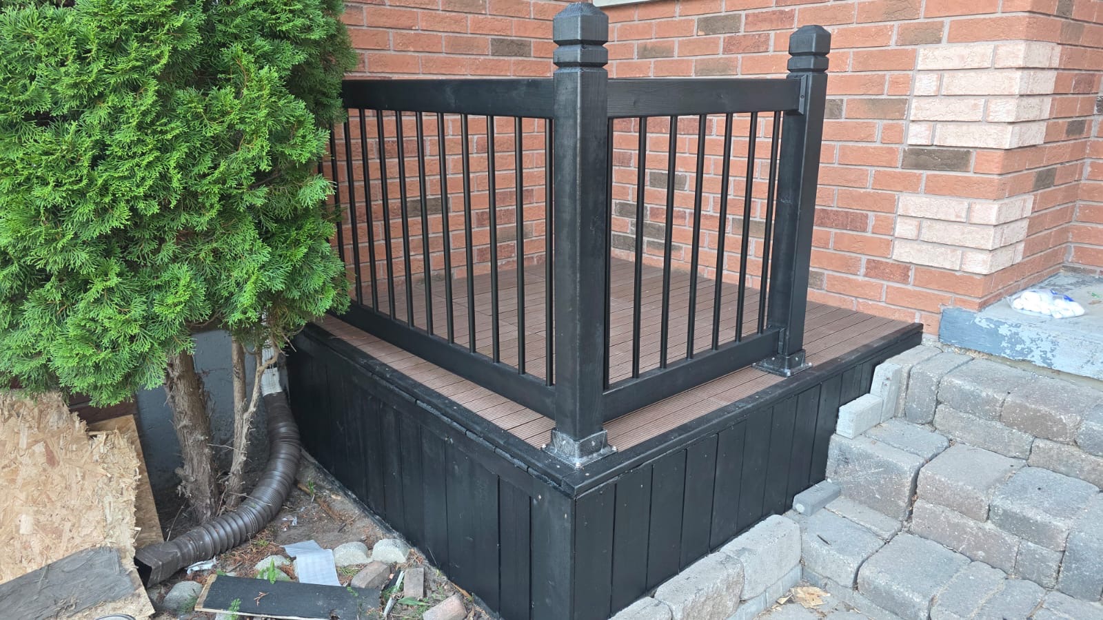 Composite porch landing with black railing and painted skirting against brick