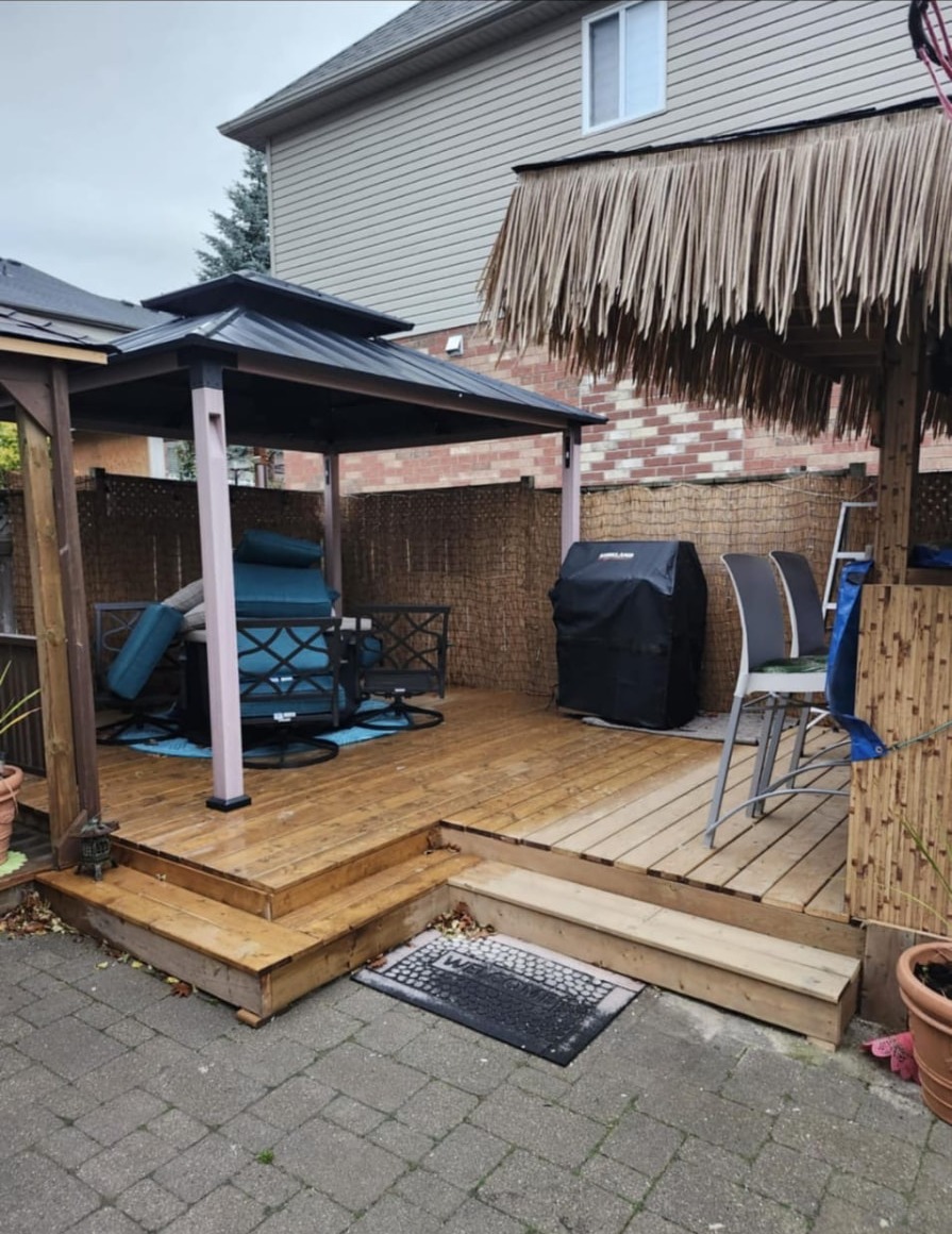 Two-tier wooden deck with metal gazebo, tiki-thatch bar overhang, and interlock stone patio