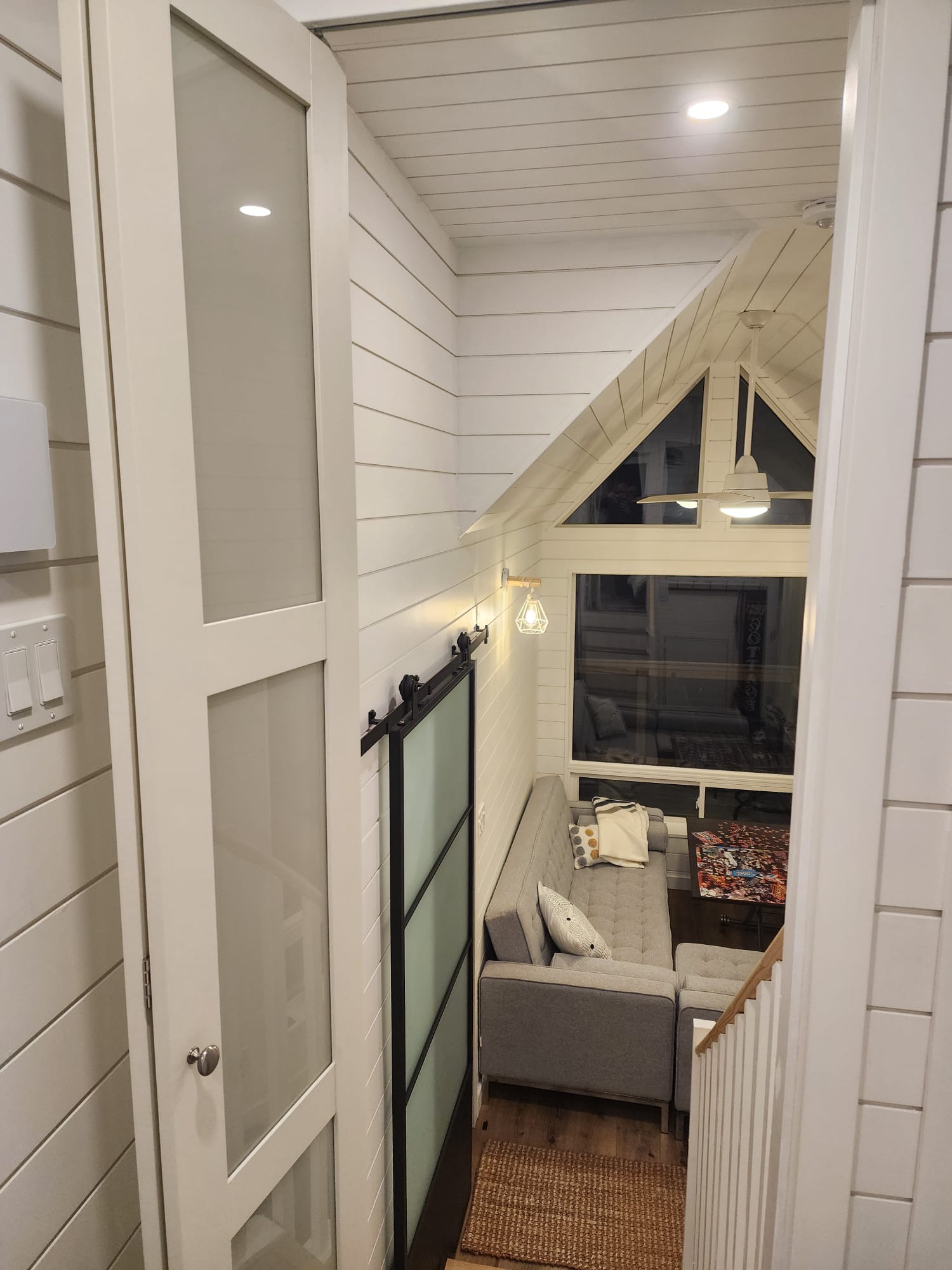 Upstairs loft landing with sliding barn door, shiplap walls, and view into living area