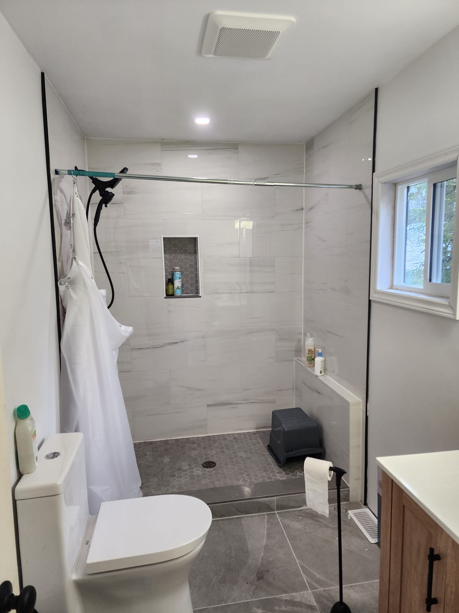Spacious walk-in shower with marble-look tile, hexagon floor, built-in bench, and window