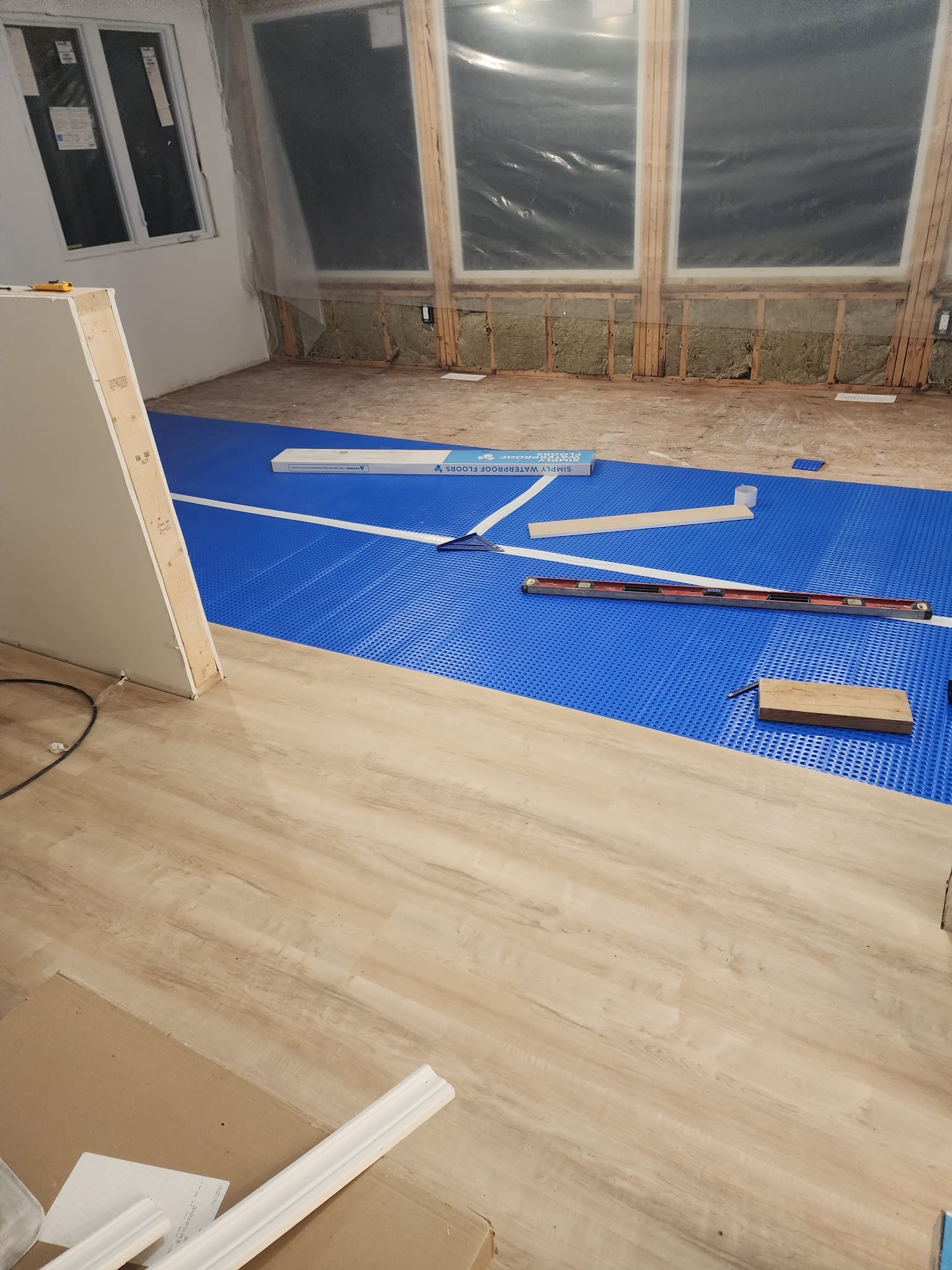 Waterproof underlayment and new plank flooring being installed in a room addition