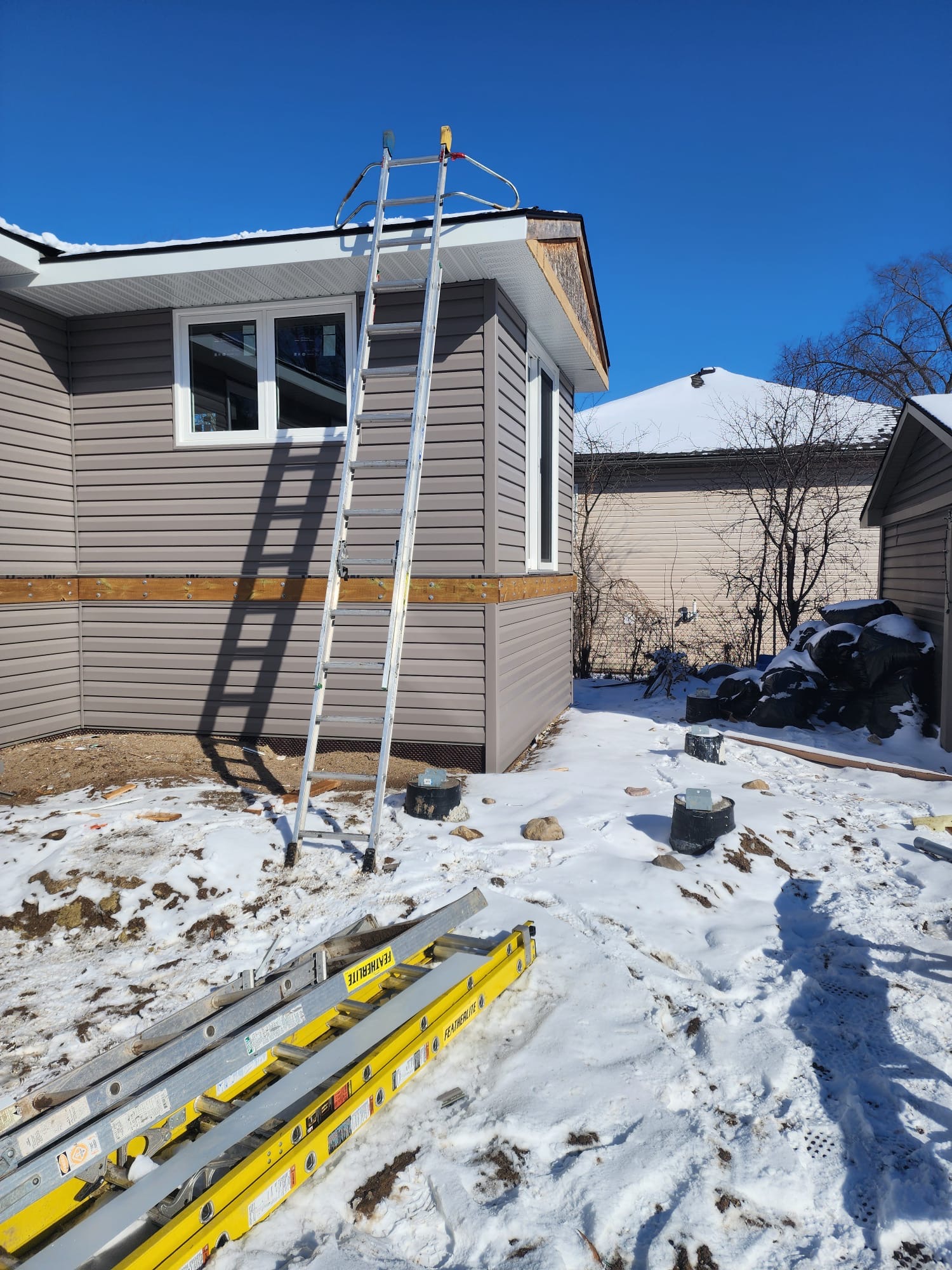 Exterior siding work on a home with ladders set up in winter snow