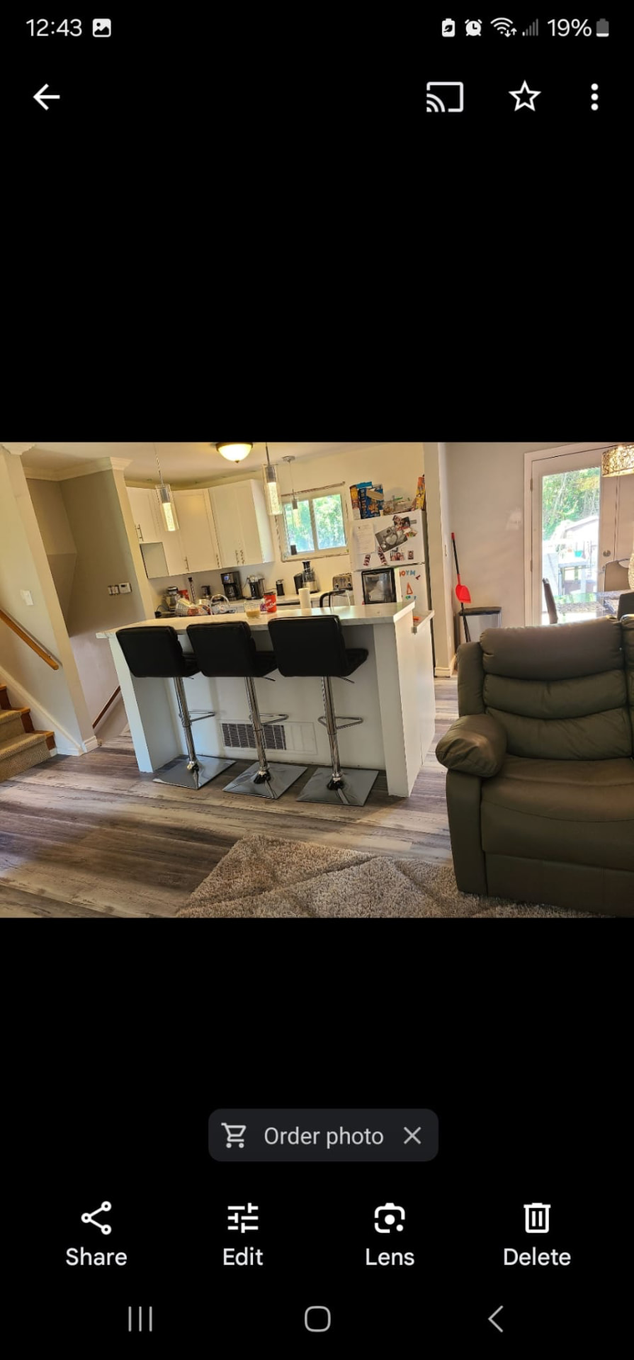 Modern kitchen with white breakfast bar, black stools, pendant lighting, and open layout