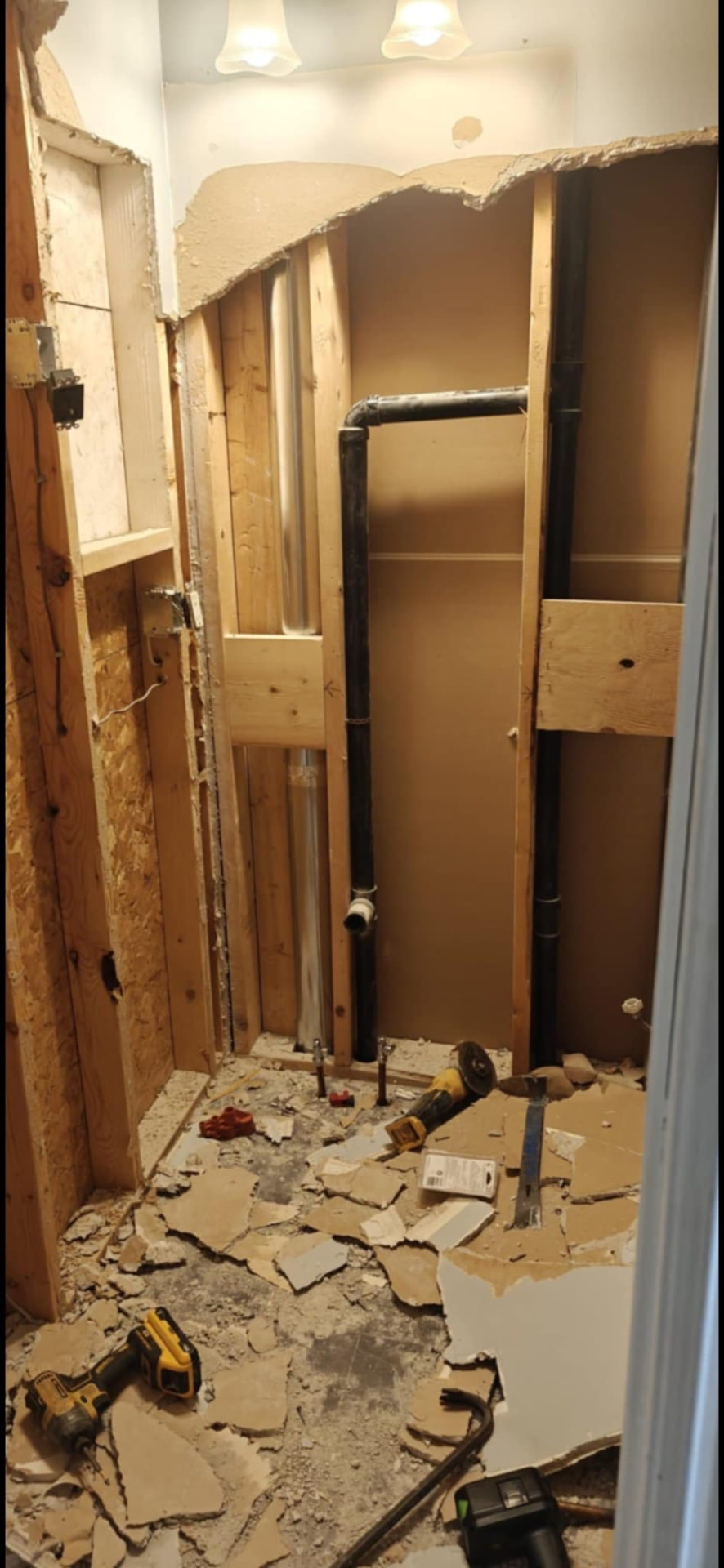 Bathroom demolition in progress with exposed studs, plumbing, and removed drywall
