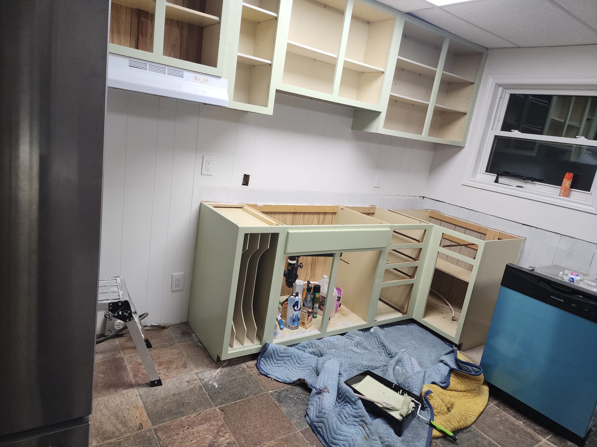 Upper and lower kitchen cabinets being painted sage green during renovation