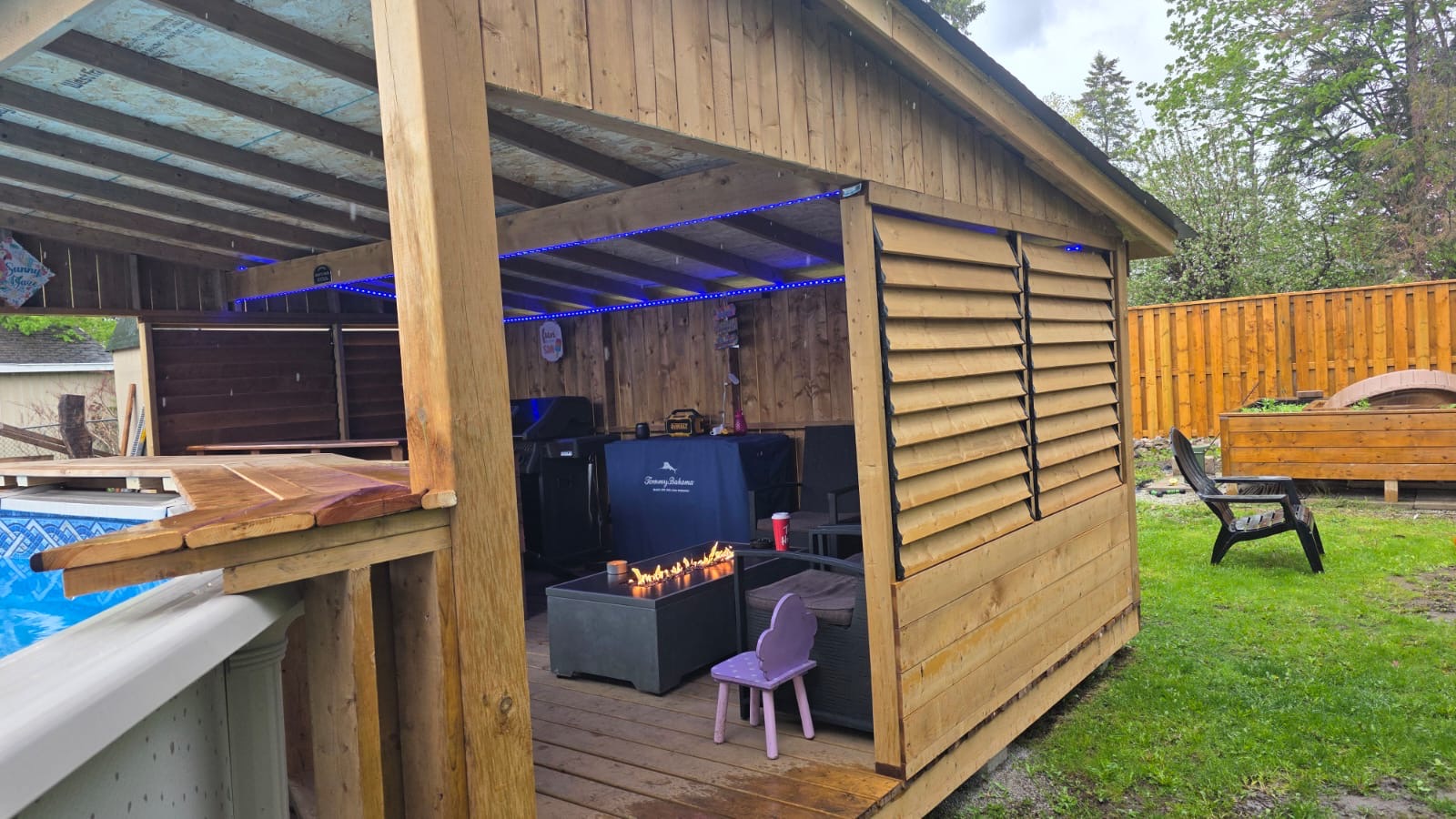 Cedar poolside cabana with louvered wall, fire table, and covered lounge area